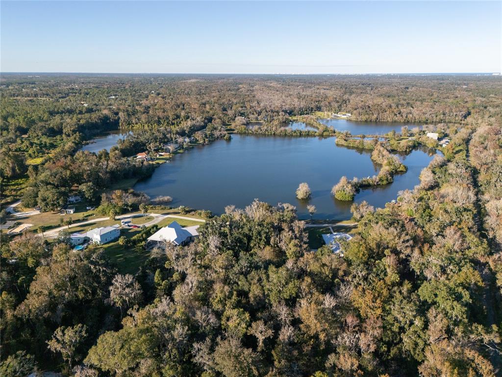 An aerial view shows a large lake surrounded by dense forest and several residential houses — 2750 PEARL LAKE TRAIL, NEW SMYRNA BEACH, FL