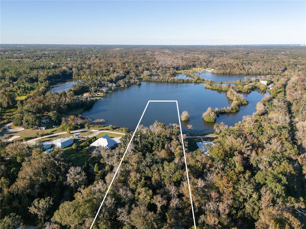 An aerial view shows a wooded lot bordering a lake with white boundary lines — 2750 PEARL LAKE TRAIL, NEW SMYRNA BEACH, FL