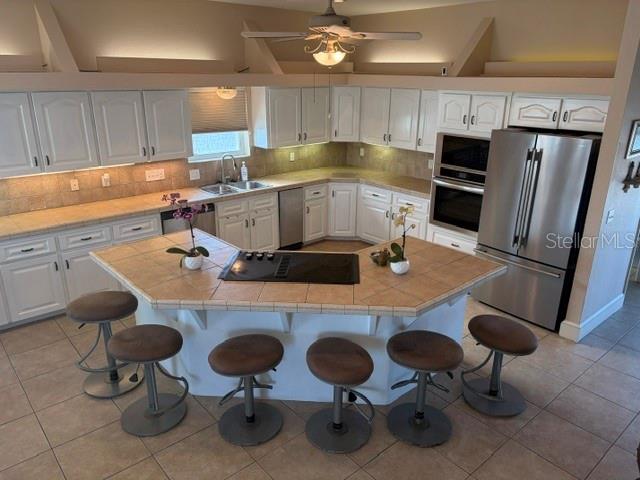 A kitchen features white cabinets, a tiled island with a cooktop, and stainless steel appliances — 6441 CLARK STREET, HUDSON, FL