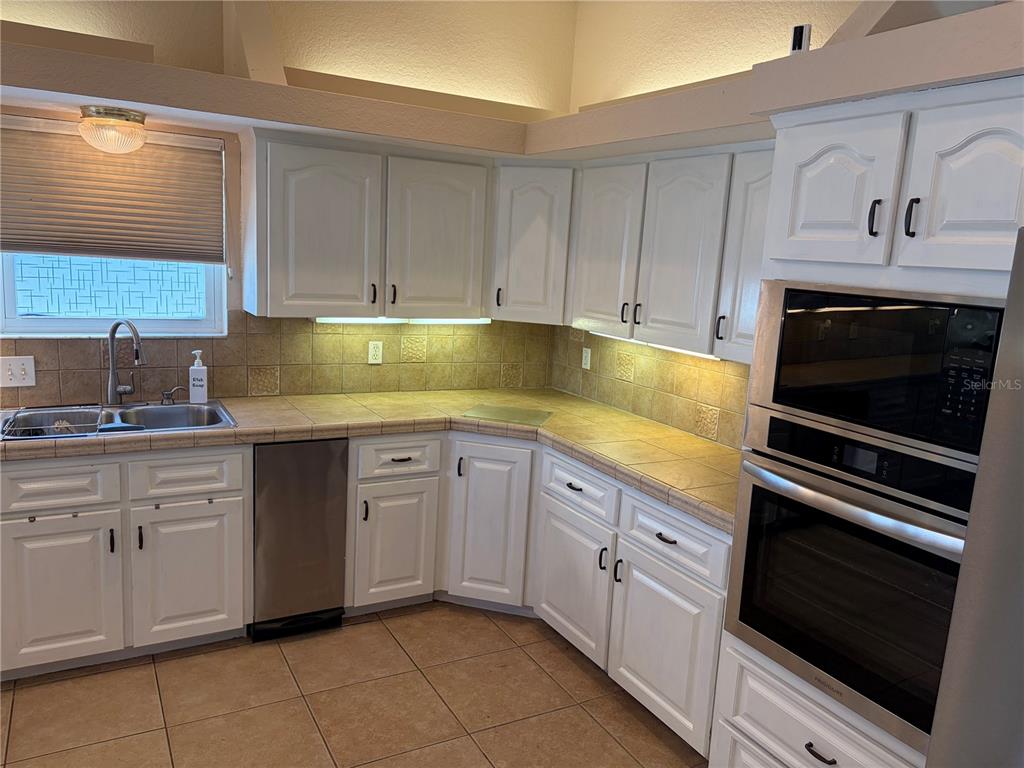 A kitchen features white cabinets, tile countertops, stainless steel appliances, and a tiled backsplash — 6441 CLARK STREET, HUDSON, FL