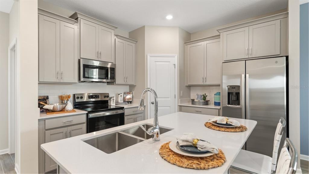 A modern kitchen features light gray cabinets, stainless steel appliances, and a white quartz island — 5650 KETTLEBELL ALLEY, CLERMONT, FL
