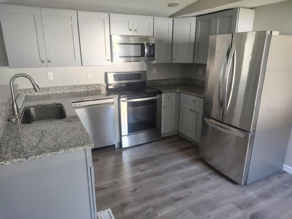 A kitchen features gray cabinets, granite countertops, stainless steel appliances, and wood-look flooring — 3940 SE 56TH AVENUE, OCALA, FL