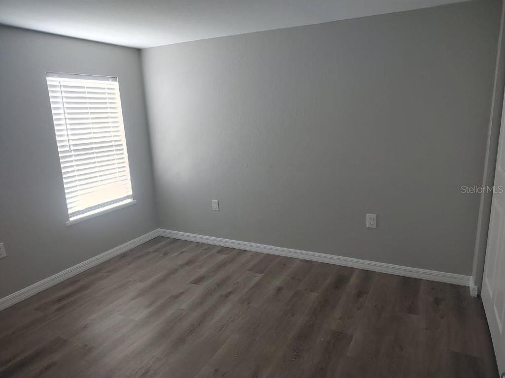An empty bedroom features gray walls, wood-look flooring, and a window with white blinds — 3940 SE 56TH AVENUE, OCALA, FL