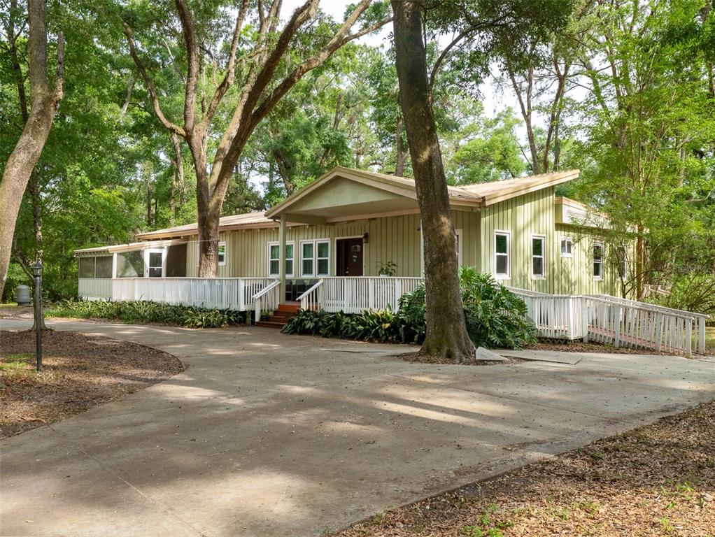 A light green house with a white deck and a ramp sits in a wooded area — 5106 SW 177TH STREET, ARCHER, FL