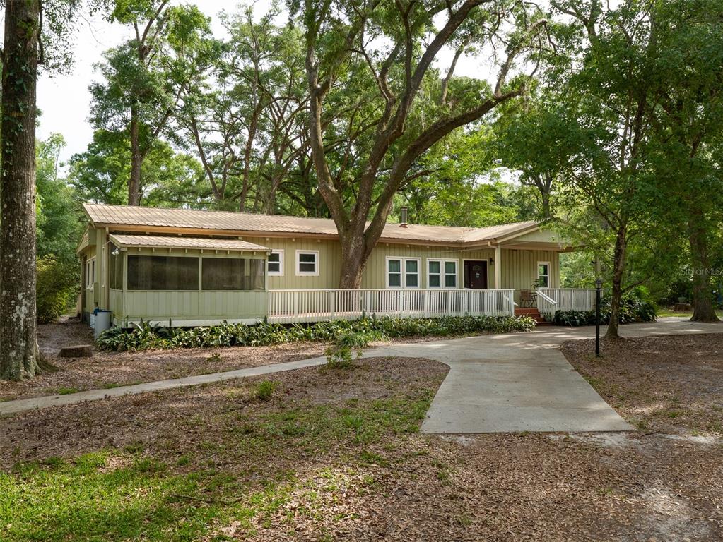 A single-story house with a metal roof, screened porch, and deck surrounded by large trees — 5106 SW 177TH STREET, ARCHER, FL