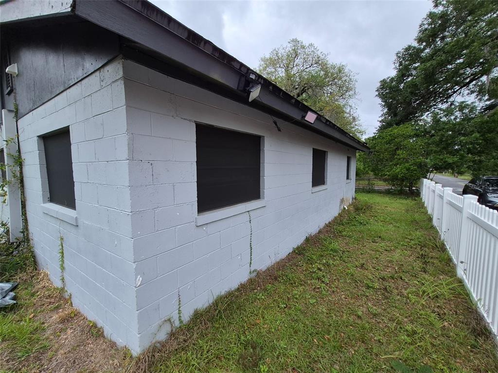 A side view of a gray concrete block house with dark window screens and fencing — 1106 SW 5TH STREET, OCALA, FL