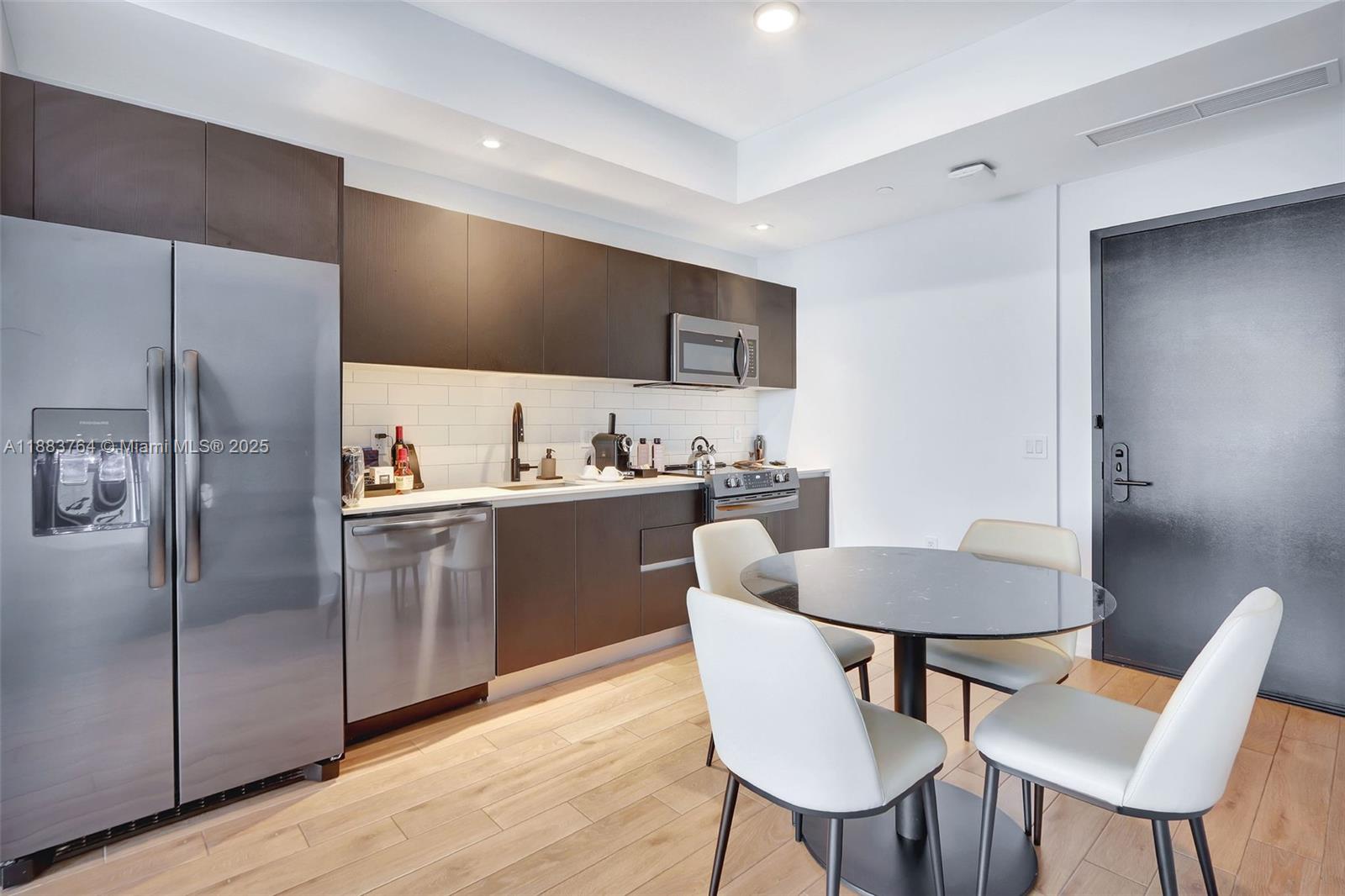 A modern kitchen features dark cabinetry, stainless steel appliances, and a small round dining table — 398 NE 5th St # 2410, Miami FL 33132, MIAMI, FL