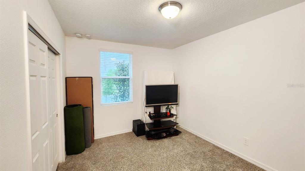 An empty bedroom features beige carpet, white walls, a window, and a television stand — 5190 MINNEOLA LANE, ST CLOUD, FL
