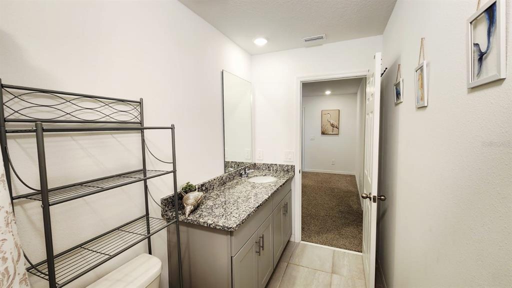 A bathroom features a granite countertop vanity, a metal shelving unit, and a doorway view — 5190 MINNEOLA LANE, ST CLOUD, FL