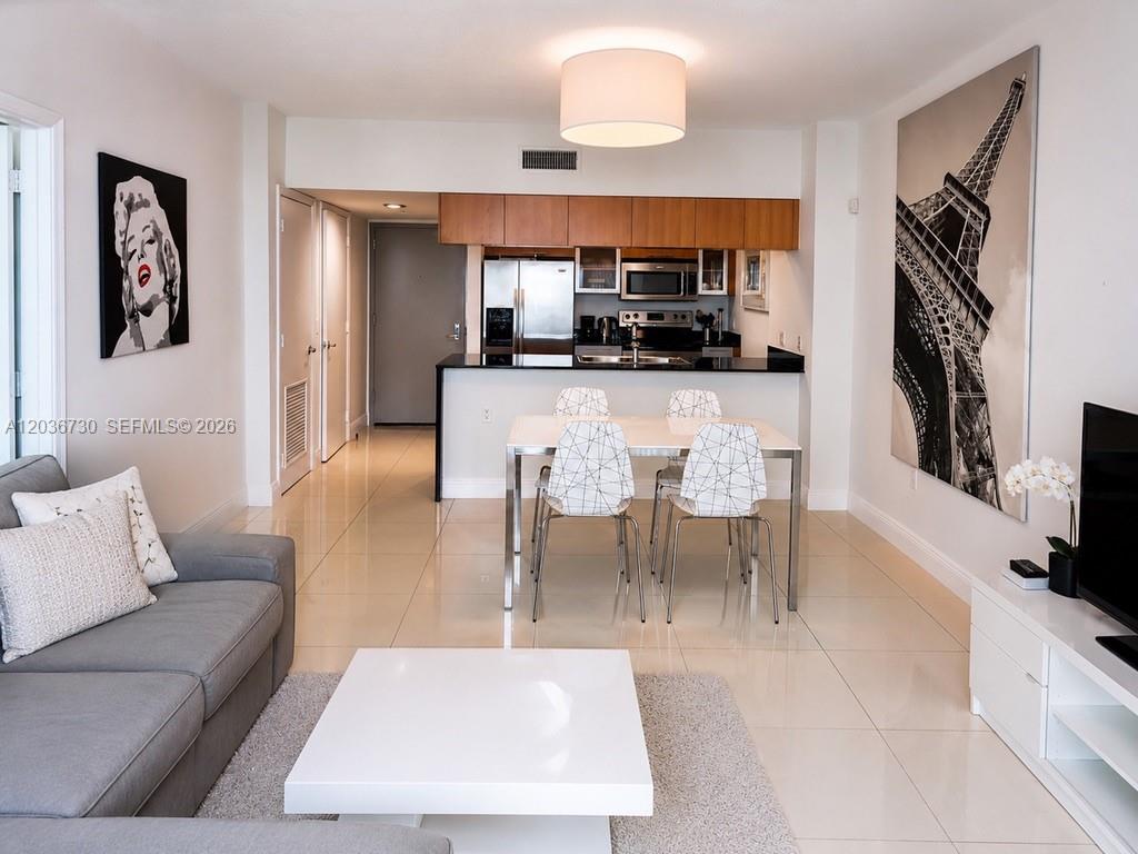 A modern living and dining area features a gray sofa, white table, and kitchen cabinetry — 1750 N Bayshore Dr # 3811, Miami FL 33132, MIAMI, FL
