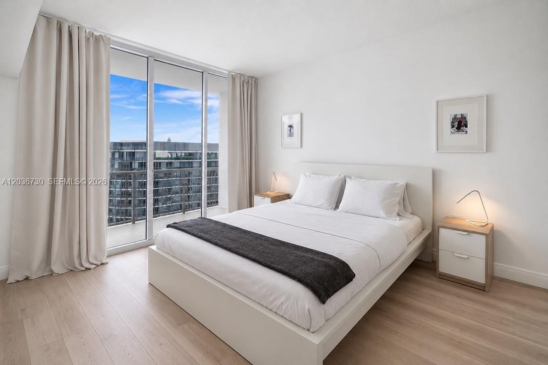 A modern bedroom features a white bed, light wood floors, and floor-to-ceiling windows with balcony access — 1750 N Bayshore Dr # 3811, Miami FL 33132, MIAMI, FL