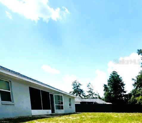 The exterior of a light-colored house features a screened-in porch and a grassy backyard — 16705 SW 22ND TERRACE ROAD, OCALA, FL