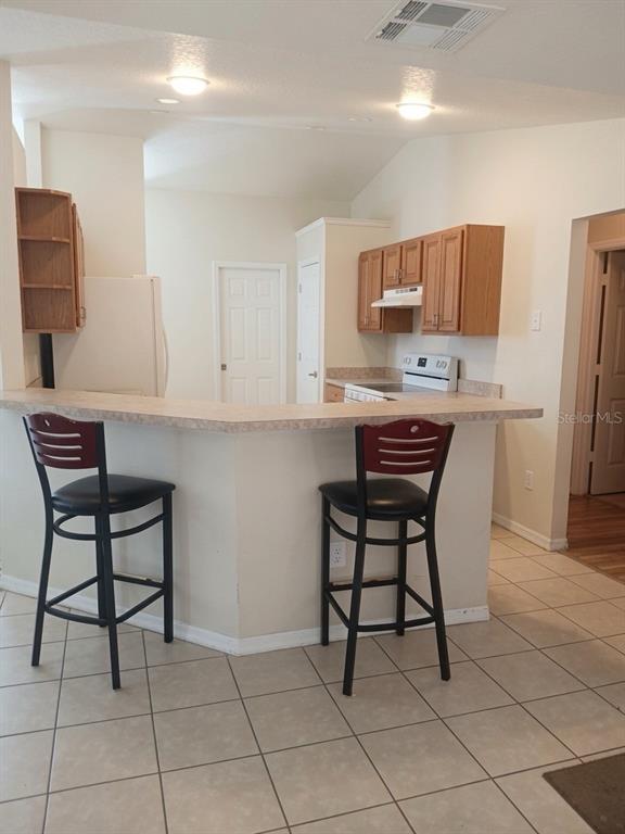 A kitchen with a breakfast bar, two stools, light-colored cabinets, and tiled flooring — 16705 SW 22ND TERRACE ROAD, OCALA, FL