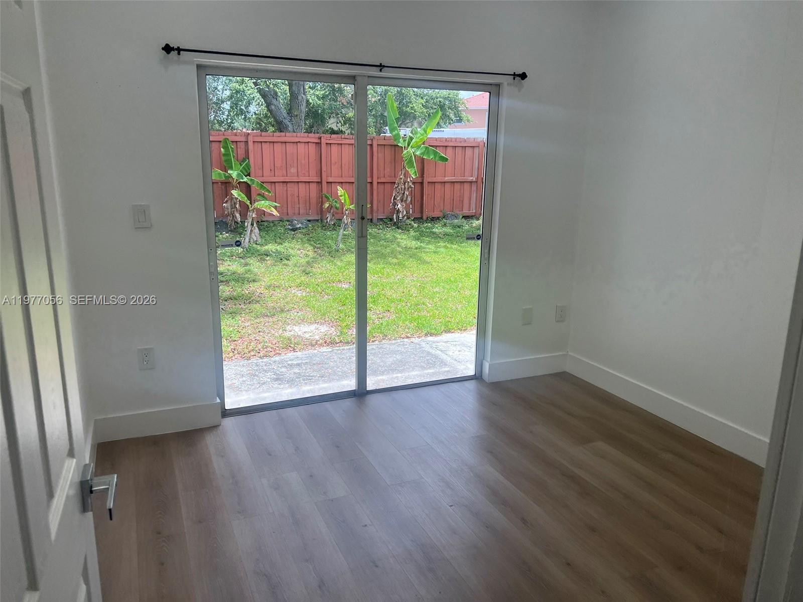 A room with light wood-look flooring and sliding glass doors opening to a fenced yard — 2511 NE 41st Ter, Homestead FL 33033, HOMESTEAD, FL