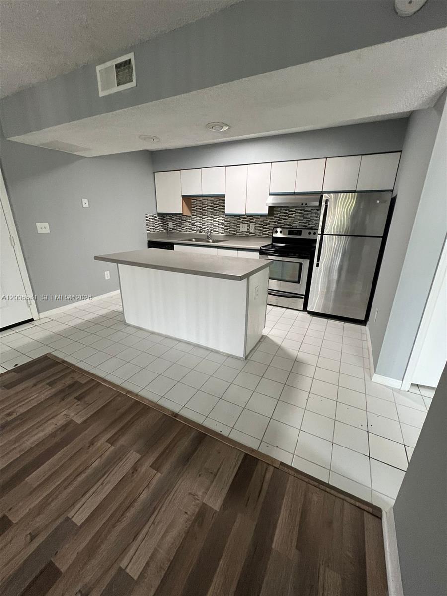 A kitchen features white cabinetry, stainless steel appliances, a center island, and tiled flooring — 3985 W Mcnab Rd # A103, Pompano Beach FL 33069, POMPANO BEACH, FL