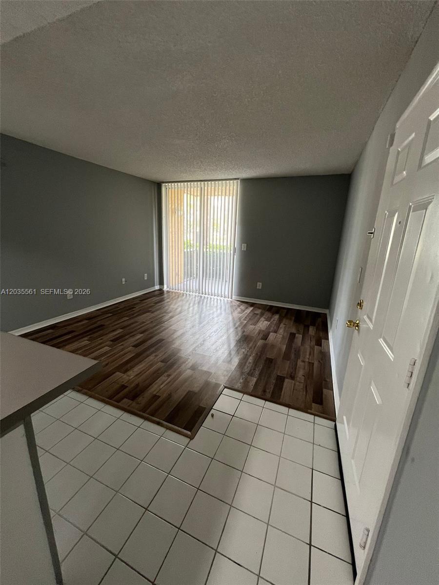 An interior view shows a living room with wood-look flooring, white tile, and sliding glass doors — 3985 W Mcnab Rd # A103, Pompano Beach FL 33069, POMPANO BEACH, FL
