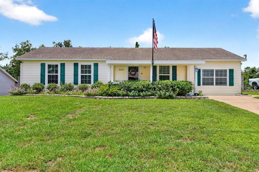 A single-story house with light siding, green shutters, and a front lawn under a blue sky — 3018 YORKSHIRE DRIVE, DELTONA, FL