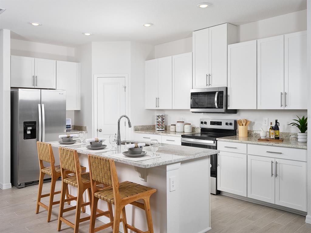 A modern kitchen features white cabinets, granite countertops, stainless steel appliances, and a central island — 14123 HARVEST PINES LANE, HUDSON, FL