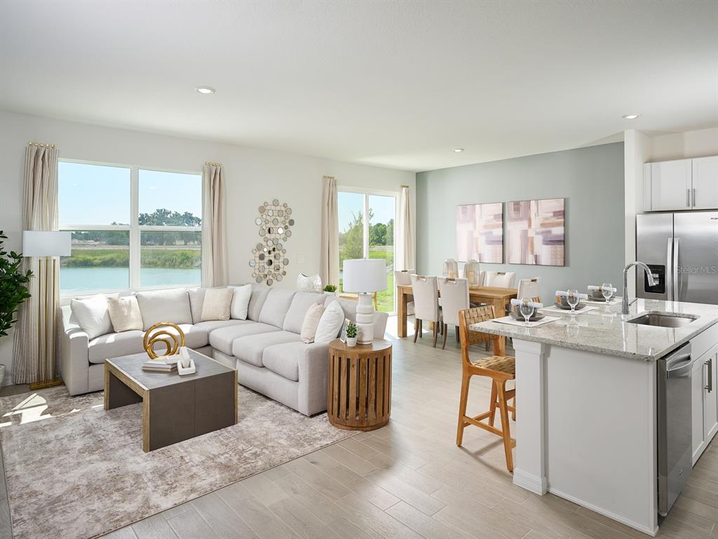 An open-concept living and dining area features light wood floors, a sectional, and water views — 14123 HARVEST PINES LANE, HUDSON, FL
