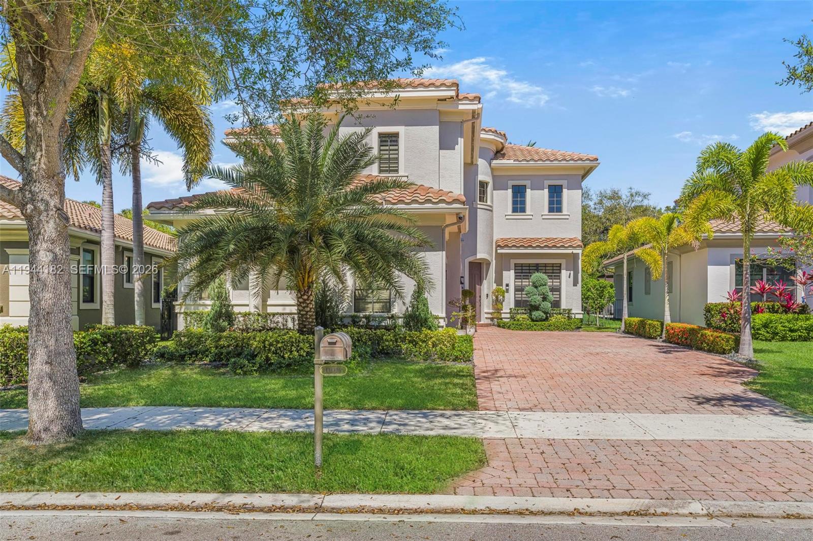 A two-story stucco house with a tile roof and a brick driveway sits behind landscaping — 10185 Cameilla St, Parkland FL 33076, PARKLAND, FL