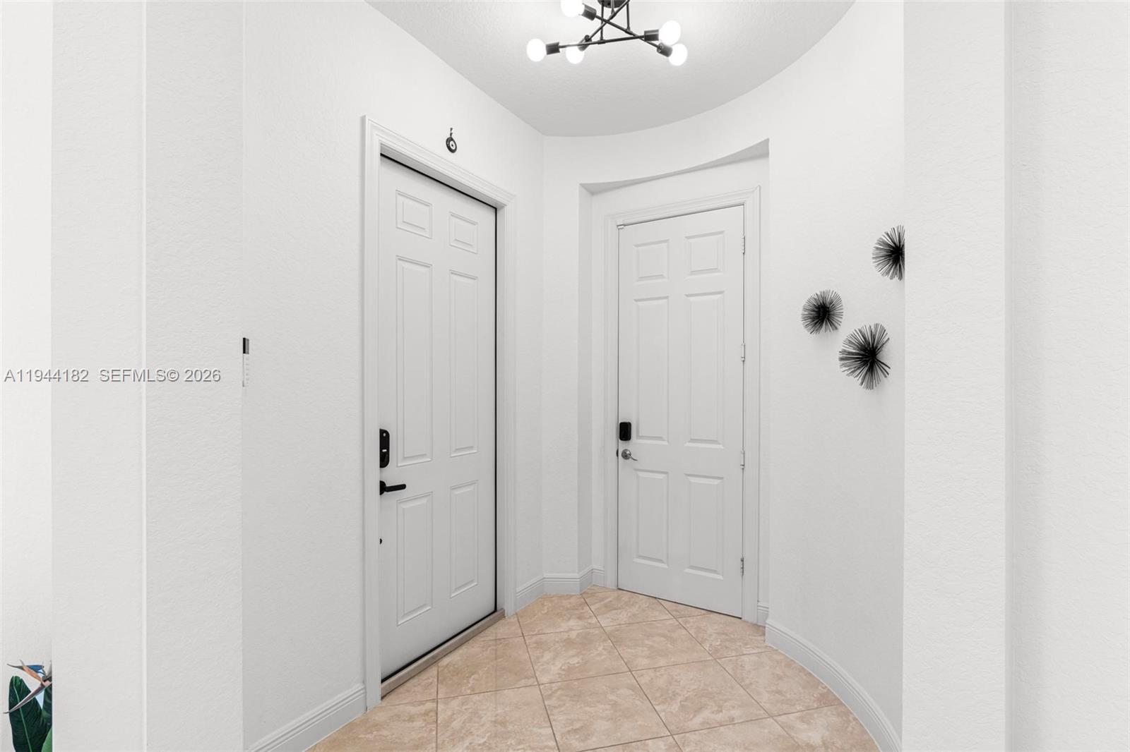 An entryway features white walls, tiled floors, two white doors, and a modern light fixture — 10185 Cameilla St, Parkland FL 33076, PARKLAND, FL