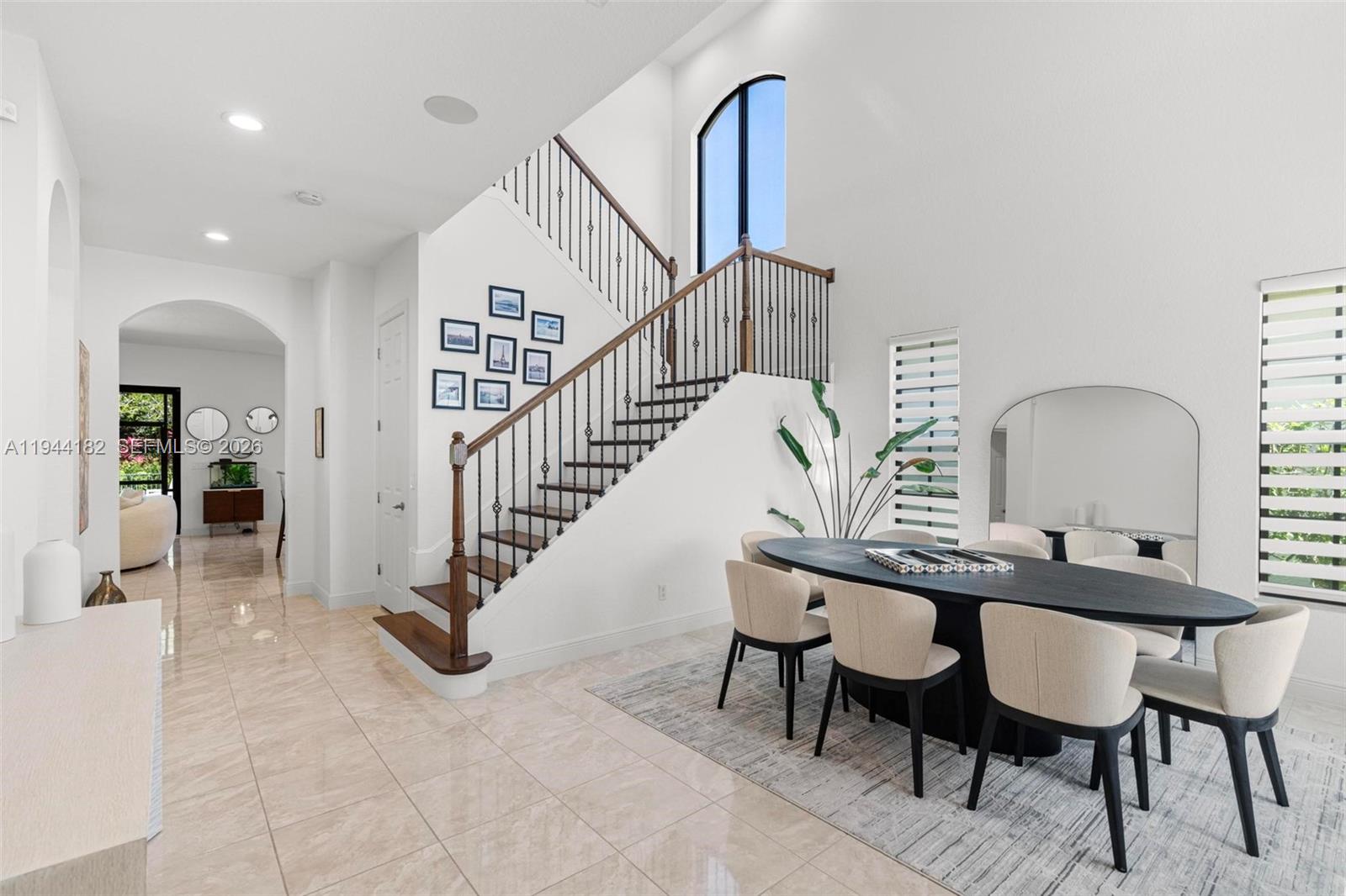 A dining area with a dark oval table sits beside a staircase with iron railings — 10185 Cameilla St, Parkland FL 33076, PARKLAND, FL