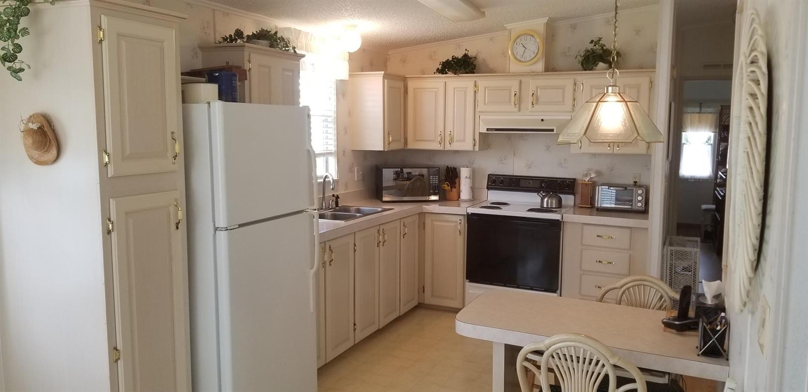 A kitchen with white cabinets, a white refrigerator, a black stove, and a dining table — 14578 Glenview Drive, Delray Beach FL 33445, DELRAY BEACH, FL