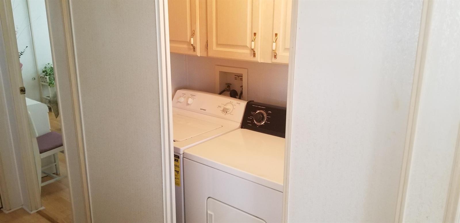 A laundry closet features a white washer and dryer beneath wall-mounted cabinets — 14578 Glenview Drive, Delray Beach FL 33445, DELRAY BEACH, FL