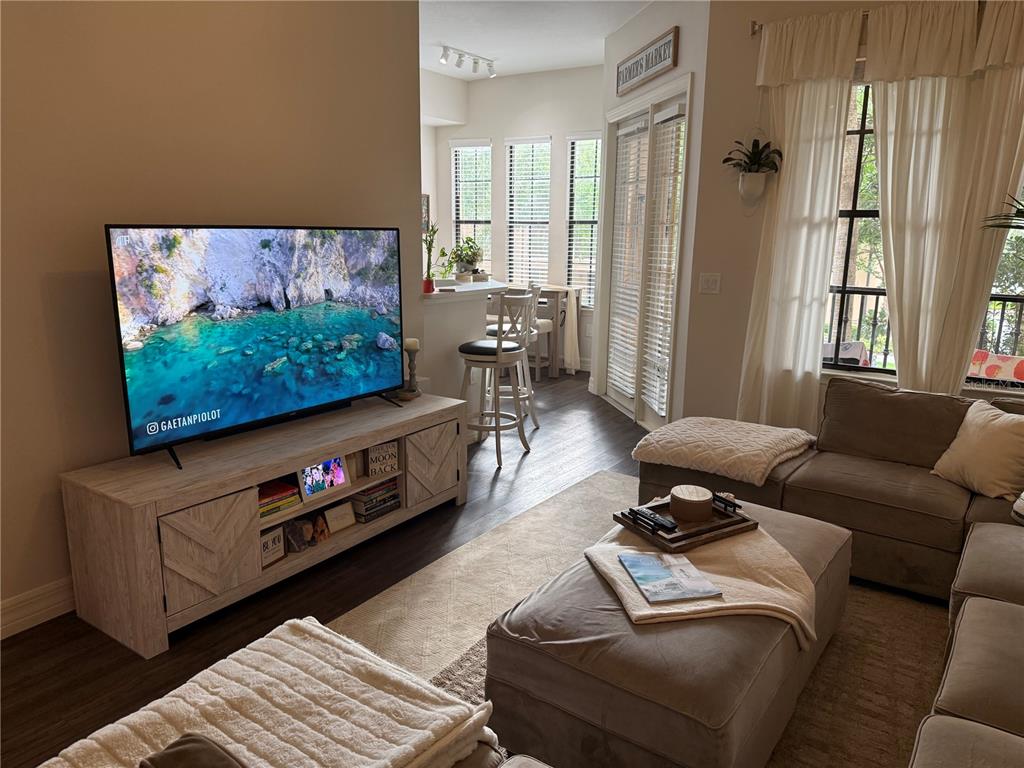 A living room features a television on a wooden console, a sectional sofa, and dining area — 513 MIRASOL CIRCLE UNIT 203, CELEBRATION, FL