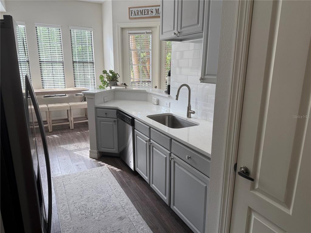 A kitchen features gray cabinets, white countertops, a stainless steel sink, and subway tile backsplash — 513 MIRASOL CIRCLE UNIT 203, CELEBRATION, FL