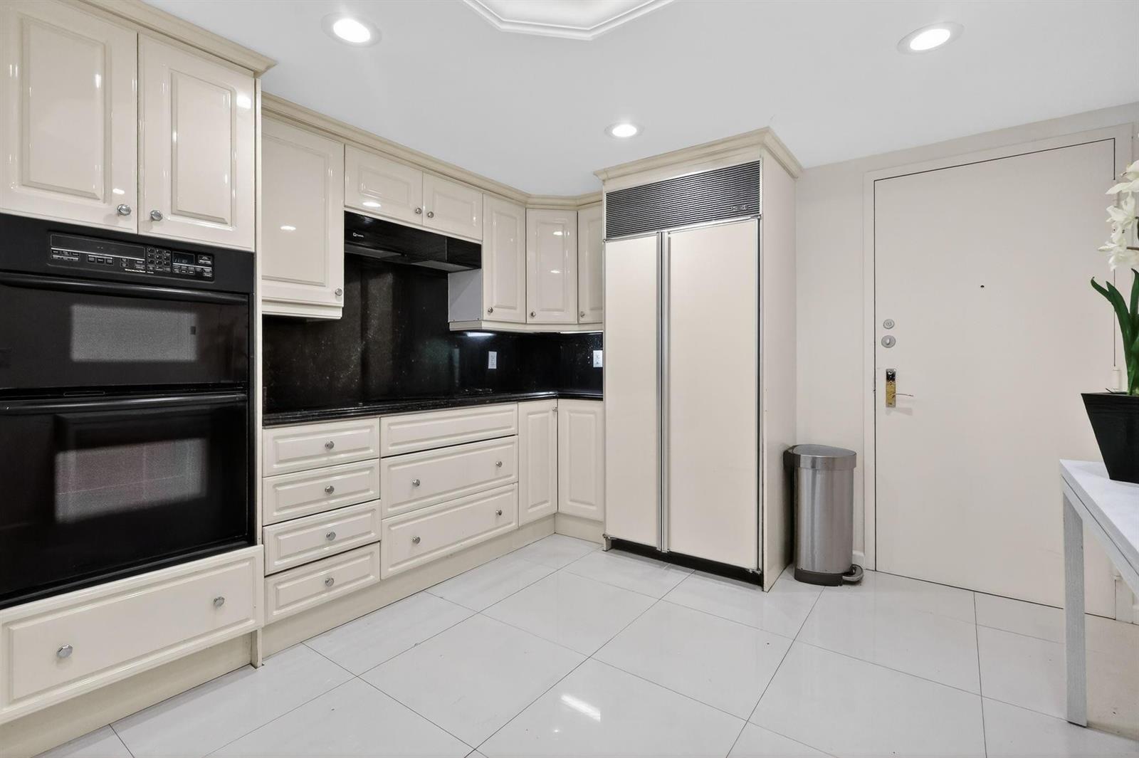 A kitchen with cream-colored cabinets, black countertops, stainless steel appliances, and white tile flooring — 9595 Collins Avenue # 8f, Surfside FL 33154, SURFSIDE, FL