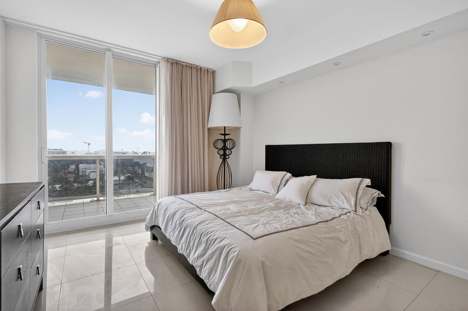 A bedroom with a black headboard, tile flooring, and a sliding glass door to a balcony — 9595 Collins Avenue # 8f, Surfside FL 33154, SURFSIDE, FL