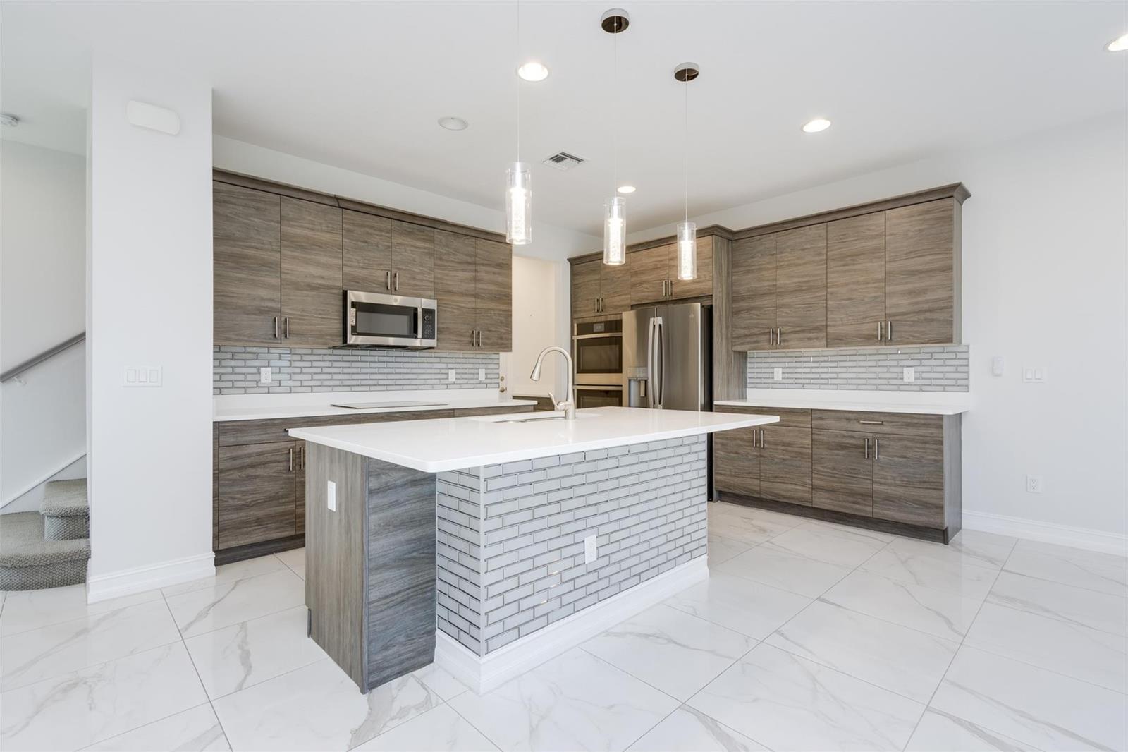 A modern kitchen features wood-grain cabinets, a brick-front island, and white marble-style tile flooring — 10124 Brickhill Drive # 10124, Boca Raton FL 33428, BOCA RATON, FL
