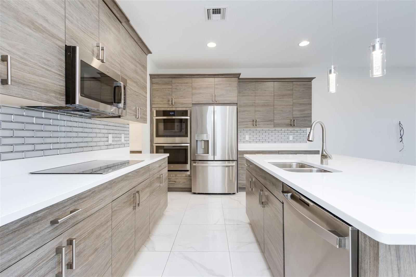 A modern kitchen features wood-grain cabinets, stainless steel appliances, white countertops, and white tile flooring — 10124 Brickhill Drive # 10124, Boca Raton FL 33428, BOCA RATON, FL
