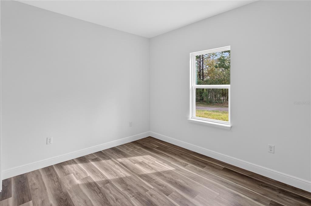 An empty bedroom features light gray walls, wood-look flooring, and a single window — 9066 N AKOLA WAY, CITRUS SPRINGS, FL