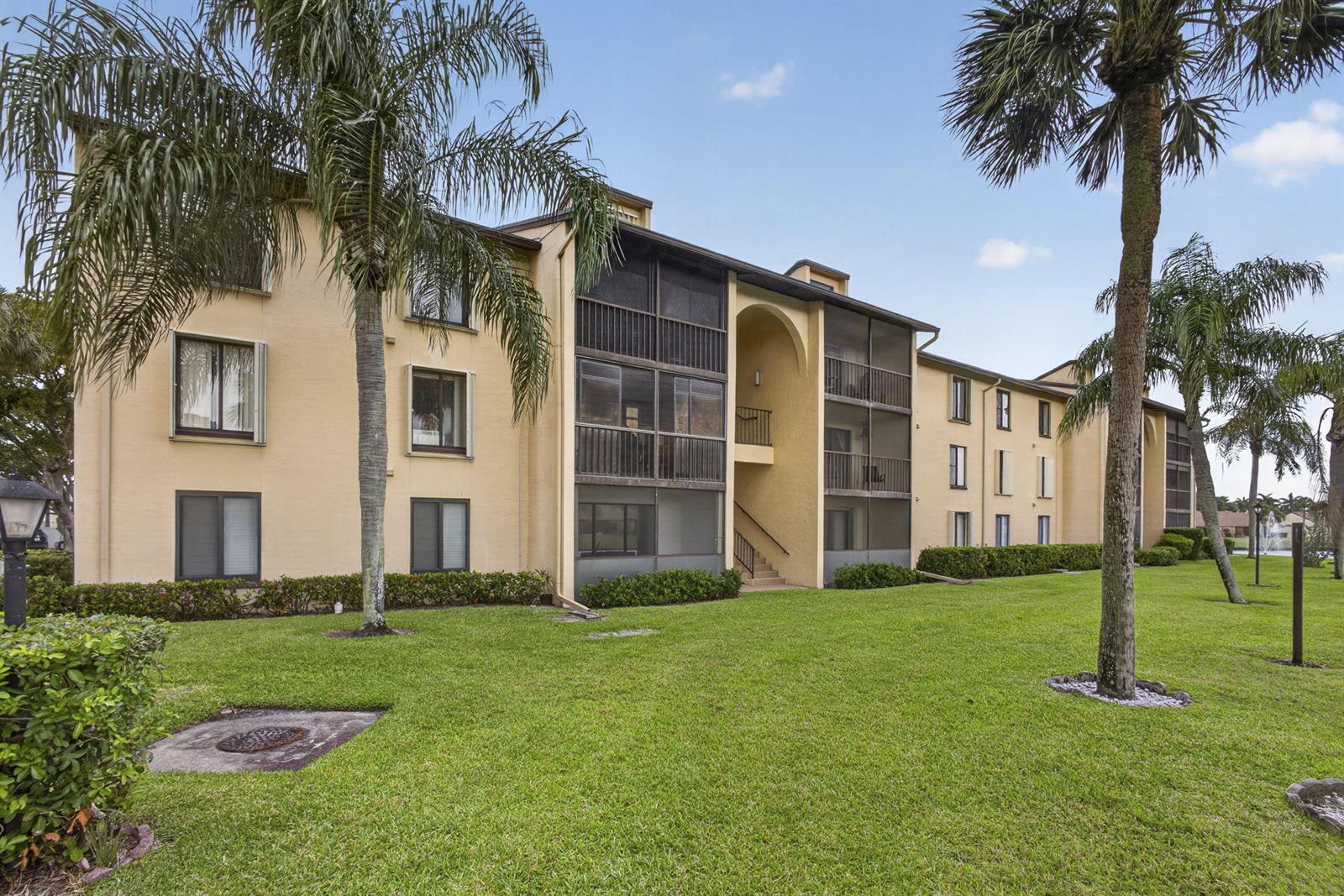 A three-story apartment building with tan stucco walls, screened balconies, and surrounding palm trees — 812 Sky Pine Way # G1, FL 33415, FL
