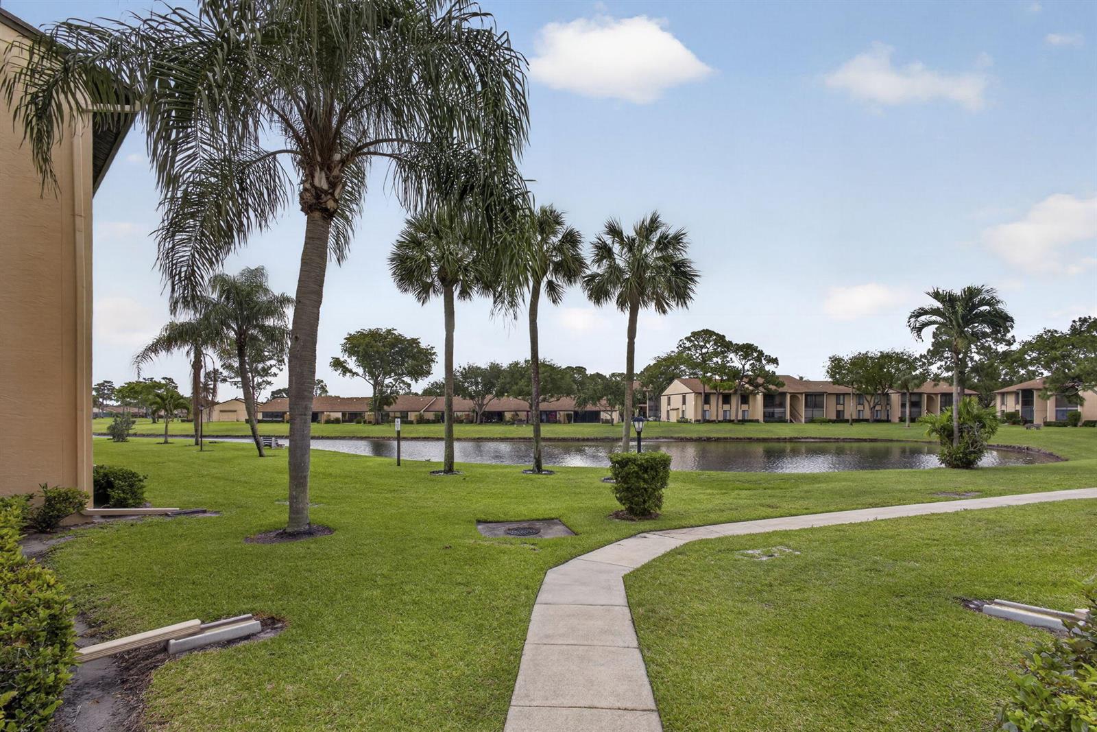 A concrete walkway leads through a grassy lawn toward a pond surrounded by palm trees — 812 Sky Pine Way # G1, FL 33415, FL