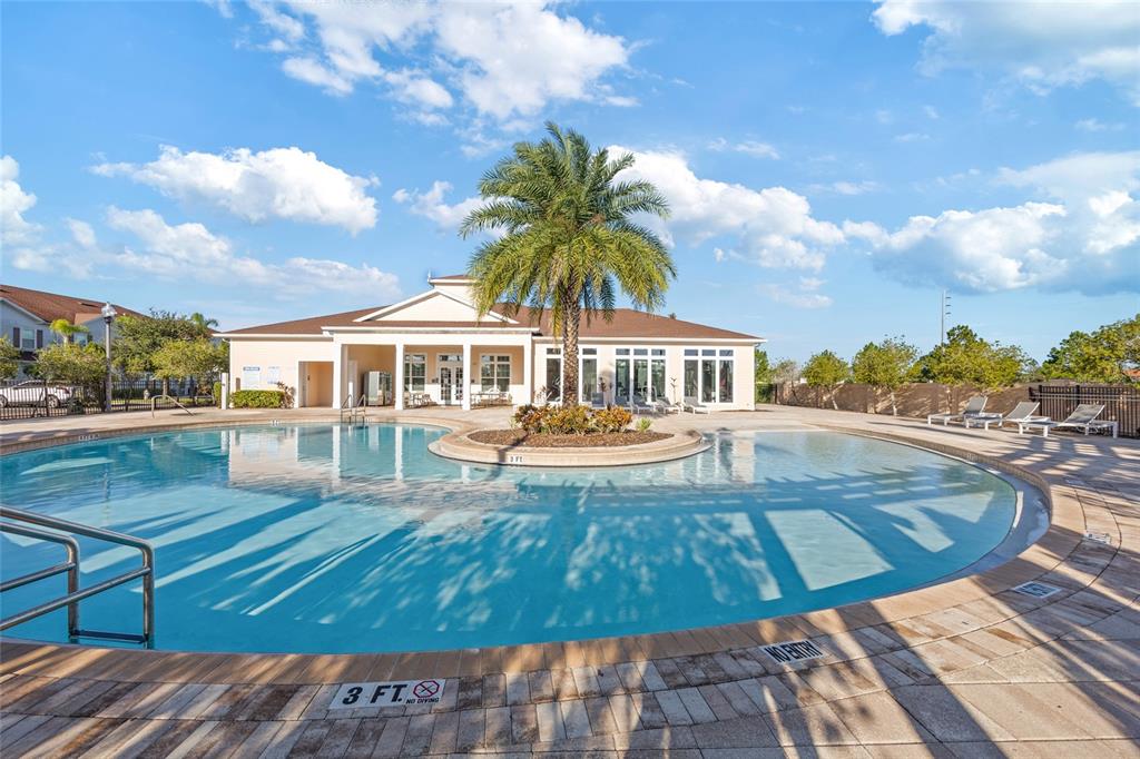 A swimming pool with a central palm tree island sits in front of a clubhouse — 8945 SHINE DRIVE, KISSIMMEE, FL