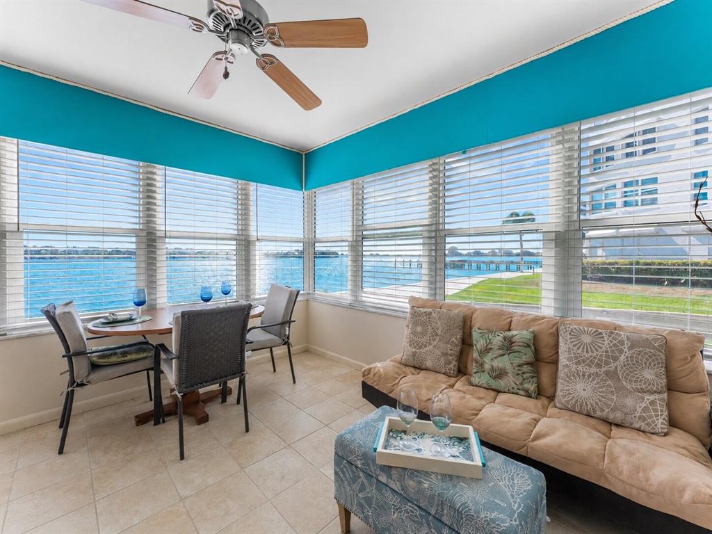 A sunroom features a dining set, a sofa, a patterned ottoman, and large water-view windows — 5020 BRITTANY DRIVE S UNIT 118, ST PETERSBURG, FL