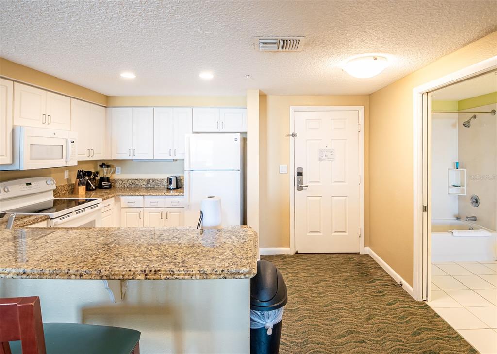 A kitchen with white cabinets and granite countertops sits next to an entryway and bathroom — 350 N ATLANTIC AVENUE UNIT 2333, DAYTONA BEACH, FL