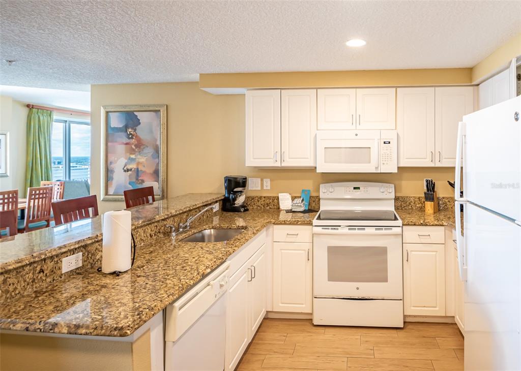 A kitchen features white cabinetry, granite countertops, a white appliance suite, and wood-look flooring — 350 N ATLANTIC AVENUE UNIT 2333, DAYTONA BEACH, FL