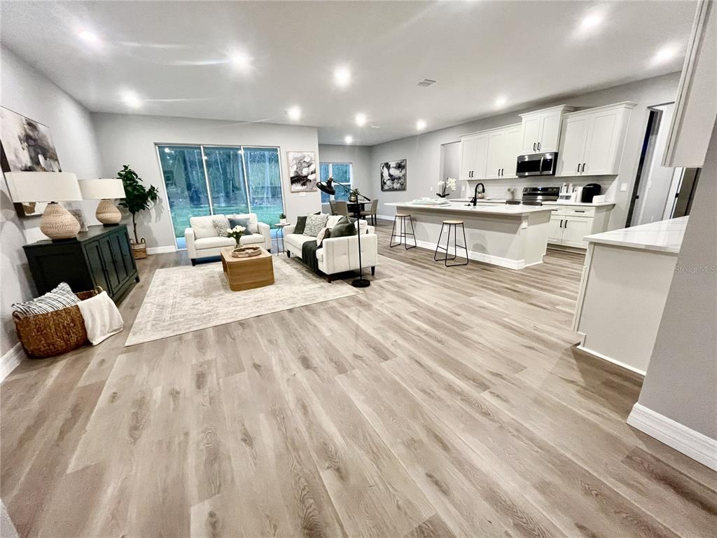 An open-concept living room and kitchen feature light wood flooring and white cabinetry — 8190 NUZUM ROAD, BROOKSVILLE, FL