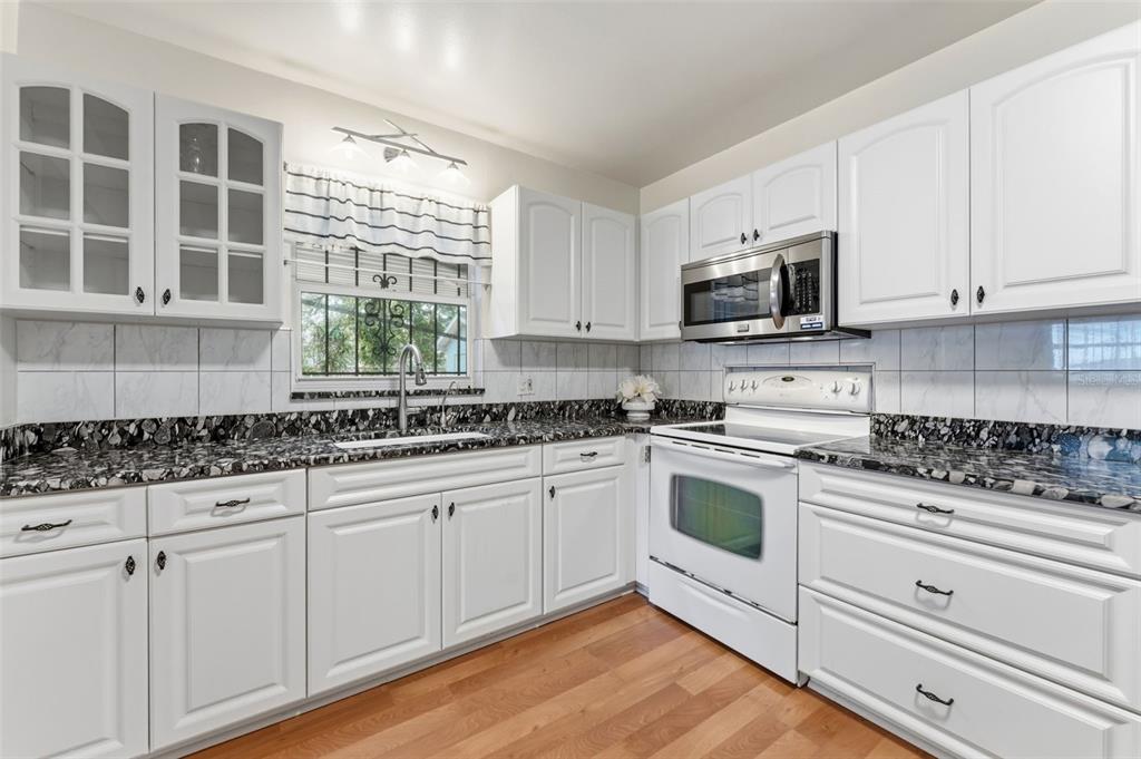 A kitchen with white cabinets, black and white granite countertops, and white appliances — 2711 W HEITER STREET, TAMPA, FL