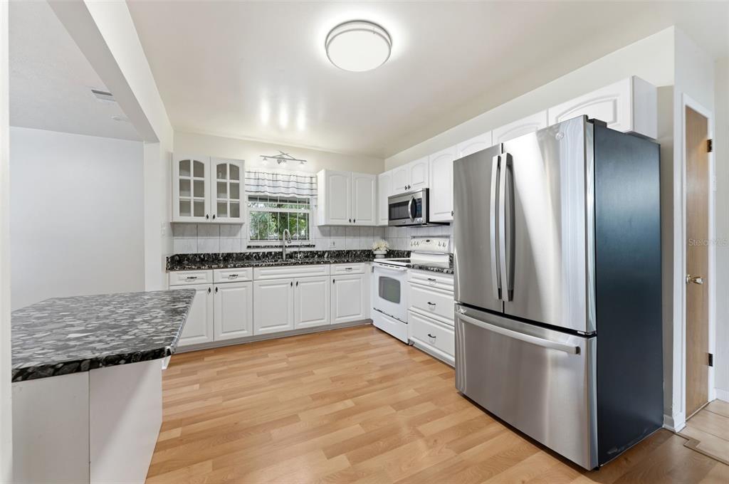 A kitchen with white cabinets, dark granite countertops, stainless steel appliances, and light wood flooring — 2711 W HEITER STREET, TAMPA, FL