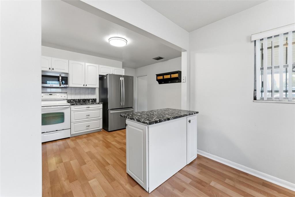 A kitchen features white cabinets, a granite-topped island, stainless steel appliances, and wood-look flooring — 2711 W HEITER STREET, TAMPA, FL
