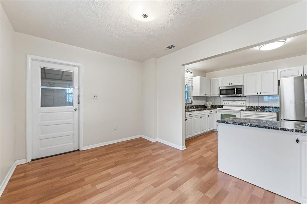 A dining area with wood-look flooring leads into a kitchen featuring white cabinets and countertops — 2711 W HEITER STREET, TAMPA, FL