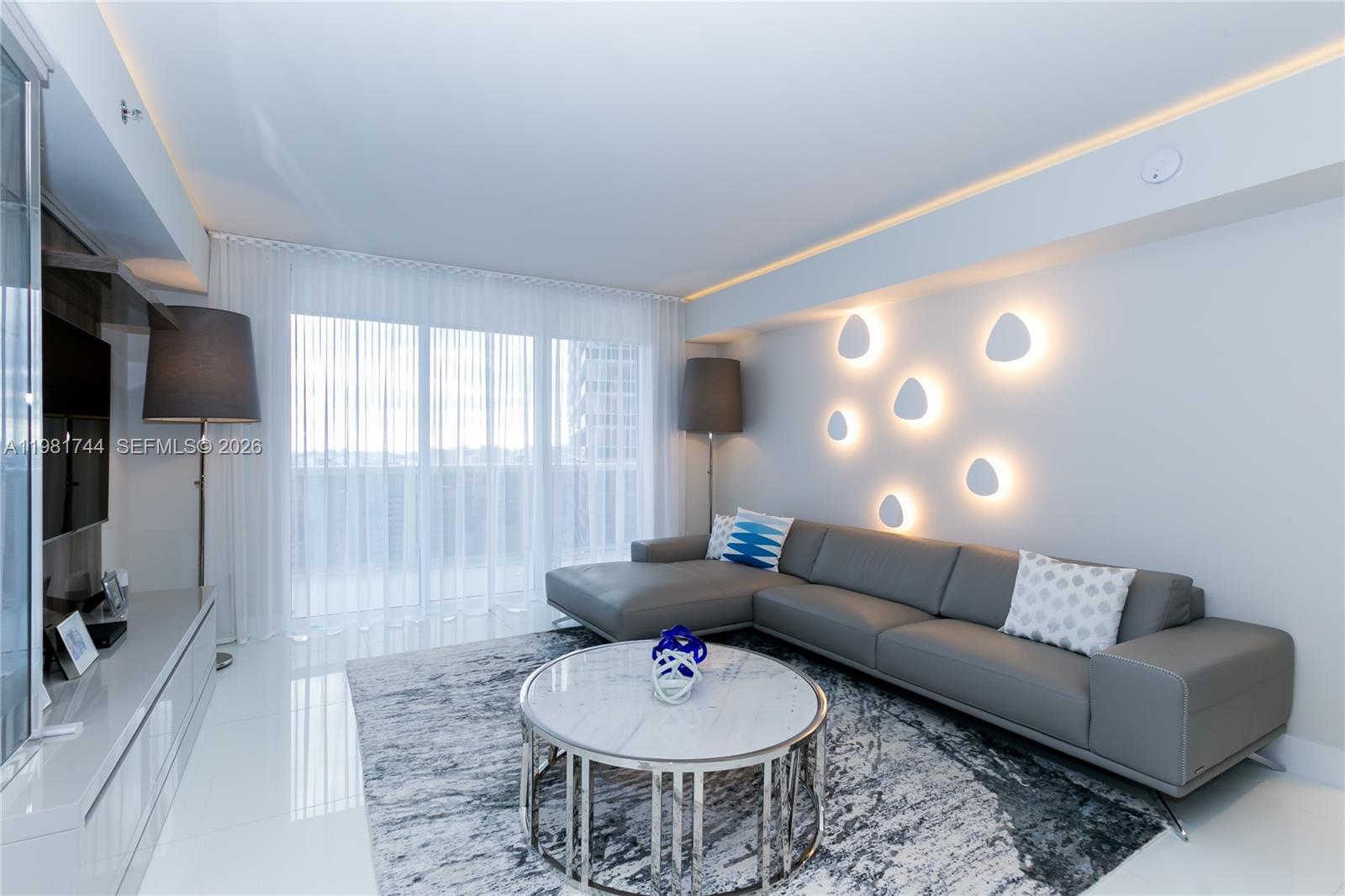 A modern living room features a gray sectional sofa, a marble coffee table, and wall-mounted lights — 1830 S Ocean Dr # 2903, Hallandale Beach FL 33009, HALLANDALE BEACH, FL