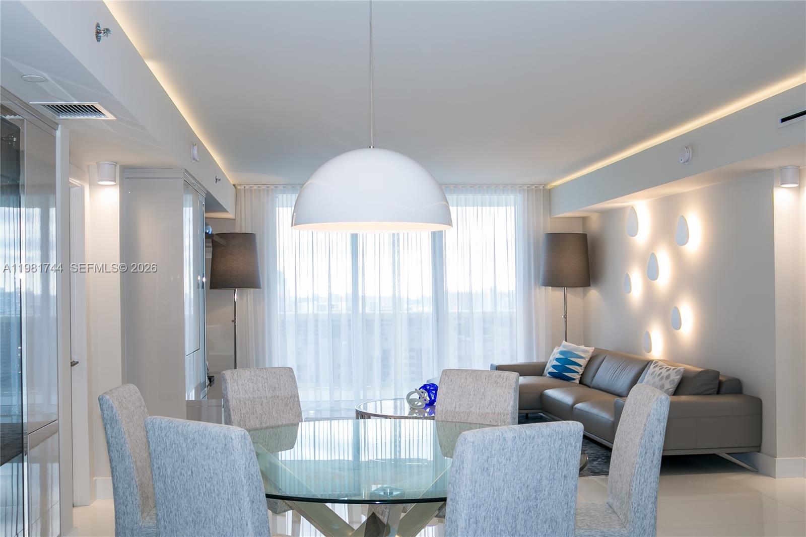 A modern dining area with a glass table and pendant light opens into a living room — 1830 S Ocean Dr # 2903, Hallandale Beach FL 33009, HALLANDALE BEACH, FL