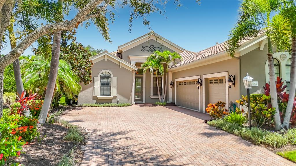 A single-story house with a brick paver driveway, two-car garage, and tropical landscaping — 7668 SILVERWOOD COURT, LAKEWOOD RANCH, FL