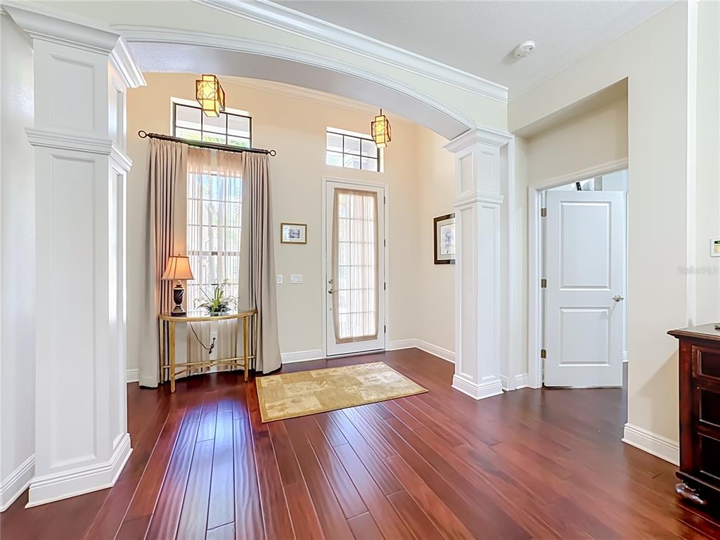 An entryway features hardwood floors, white columns, an arched ceiling, and a front door — 7668 SILVERWOOD COURT, LAKEWOOD RANCH, FL